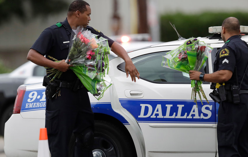 Two police officers standing in front of a police car hold flowers they were given.