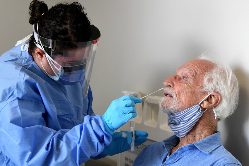 A medical professional inserting a nasal swab into an older man's nose.