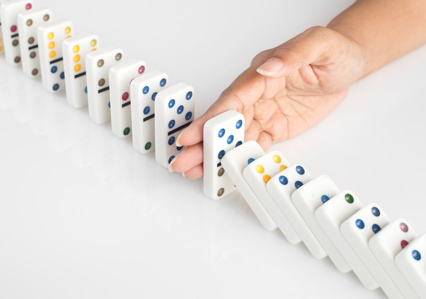 Human hand stopping a line of dominoes from falling. concept image for recovery plan and solution for cascading failures and problems. Dominoes are placed on a white table.