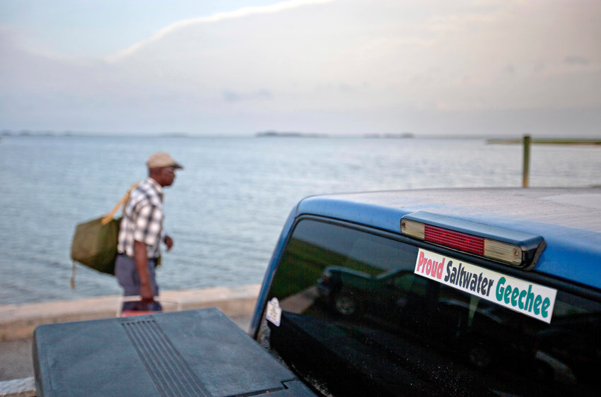 A sticker celebrating the Geechee heritage is seen on a pickup truck as passengers board a ferry.