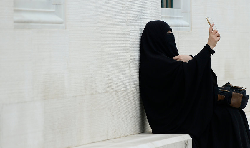 A covered Muslim woman is taking a selfie while seated on a bench