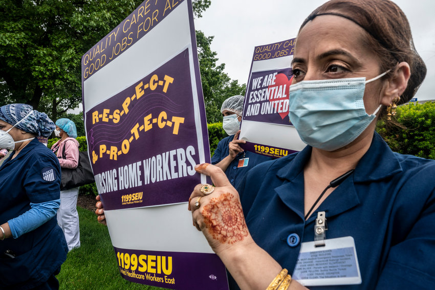 A nursing assistant with a badge holds a sign reading: Respect, Protect Nursing Home Workers