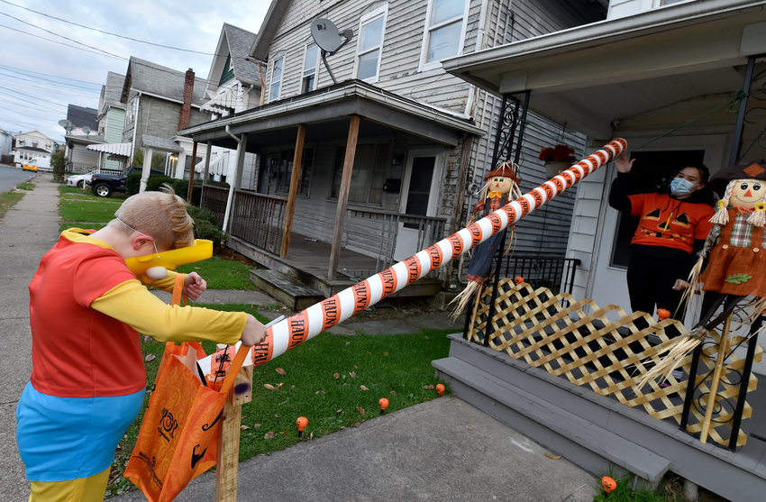 A woman wearing a face mask sends candies down a chute to a boy trick or treating