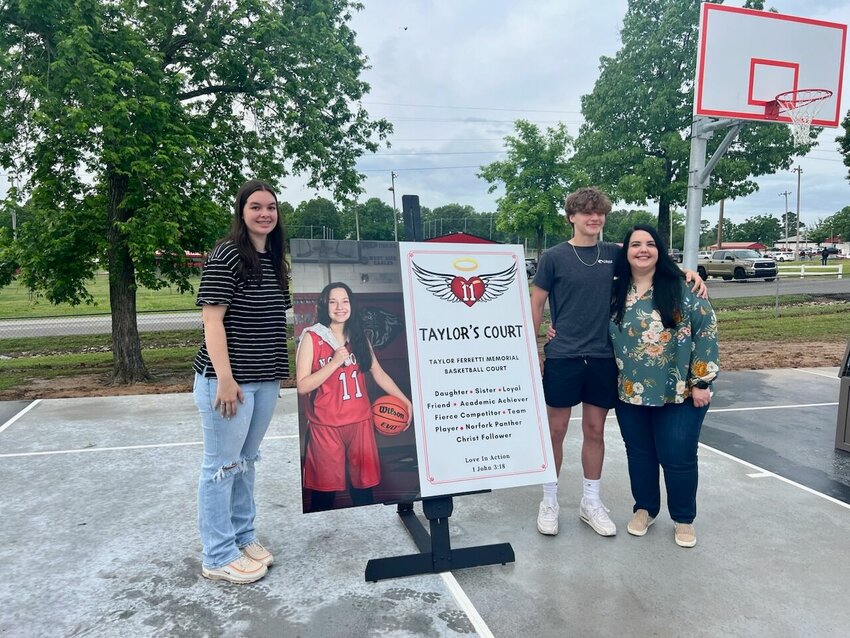 Taylor Ferretti's best friend, Jenna; brother Ryker; and mother Stacey stand beside the memorial court sign that will be displayed on the Arrie Goforth Elementary School playground in Norfork.


Submitted Photo