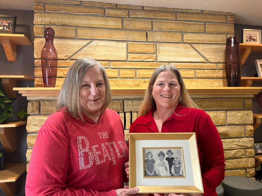 Joan (Riley) Young (left) and Jill (Riley) Holman pose with a photo of themselves in front of their old home fireplace in the house they grew up in, now known as the Schliemann Center for Women. Baxter Regional Health System (as it was known when the property was acquired) purchased the home and two others as part of their off-campus expansion to provide services and resources to those in need within the community. Young and Holman continue to be a part of the home's legacy and the support it provides for women in the area.   Caroline Spears/The Baxter Bulletin