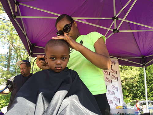Free haircuts were a popular attraction at the many booths at the block party. DeDee Davis trims the hair of young Mahlik Gentry, age 3. JOE WESTBURY/Index