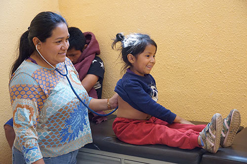 Fiver-year-old Charon smiles during a medical checkup for respiratory issues at the Guatemala City Dump School and Clinic in Guatemala. Respiratory illnesses for those who live near the dump, such as Charon and her mother and siblings, are commonplace for those receiving aid from IMAP. IMAP/Special