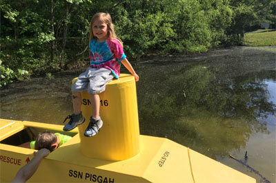 Channing Gladson, daughter of Brad Gladson who owns the pond where the submarine is being tested, sits atop the hatch while Steve Phillips, in green shirt, checks out the interior. MOUNT PISGAH/Special