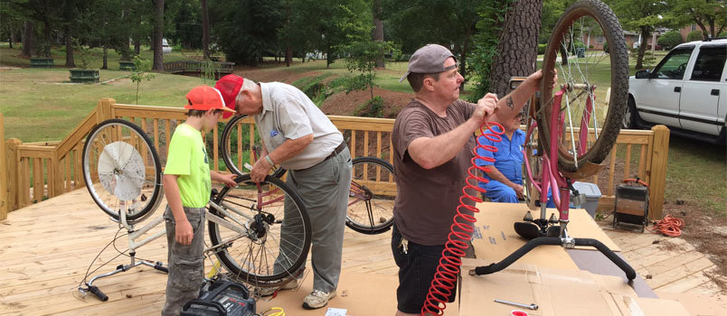 Young Riley Newsome, left, helps Ted Jarriel administer a patch while Joe Lausch pumps up a tire on another bicycle tire. Darrel Holliday, seated, waits to welcome more bicycles to be dropped off for minor repairs as part of Jefferson Street Baptist's Summer of Service. DARREN TALLEY/Special