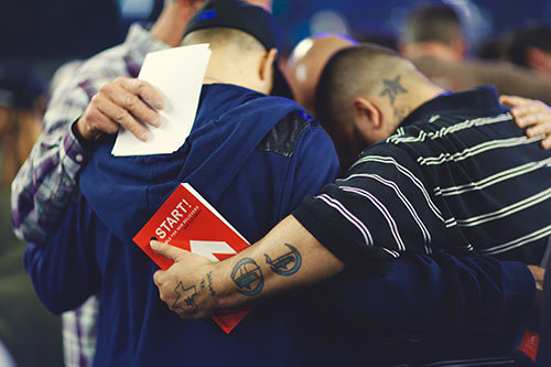 Men pray together after making professions of faith in Christ at the Harvest Crusade in Dallas, TX. While 6,500 made a faith commitment at AT&T Stadium, 18,000 more responded likewise at sattelite locations. TREVER HOEHNE/Harvest Ministries