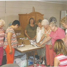 Members of Crafters for Christ pray over items available for free to attendees at the Georgia National Fair. The group meets weekly at Smith Baptist Church in Vidalia and create items with a Scripture verse attached. In addition to items such as huggy bears, patriotic keyholders, and bookmark crosses, the group provided a cup of water to each guest and gospel tract.