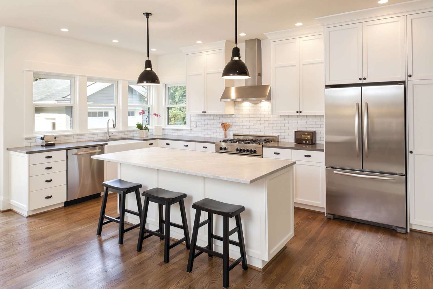 This is a fairly typical kitchen renovation, by modern standards: white cabinets, open space, center island with pendant lights, stainless steel appliances and white subway-tile backsplash.