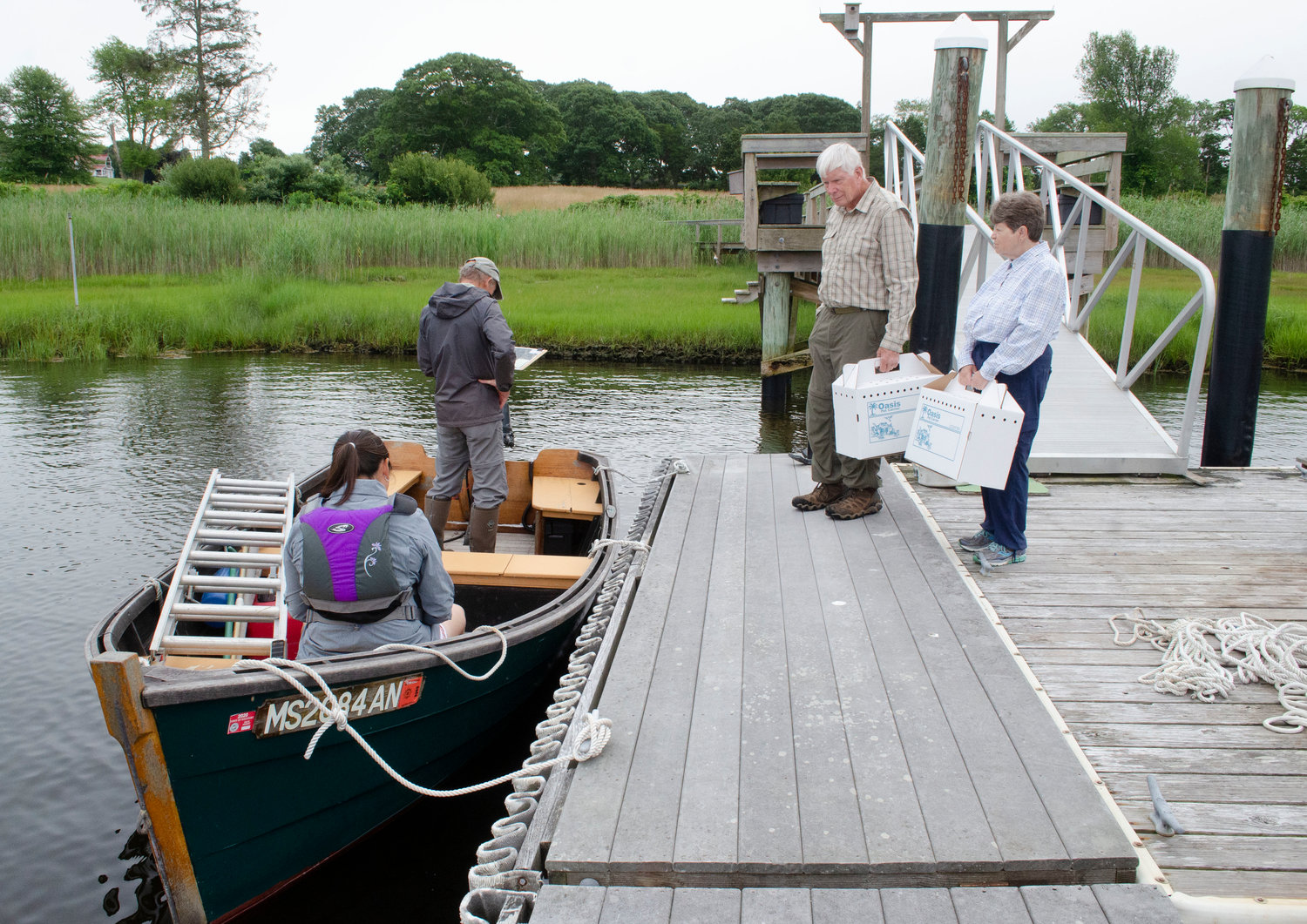 At the dock, Dr. Alan Poole (left) and Tih-Fen Ting ready the boat and look for the location of the first osprey while volunteers Judy and Harold Isaksen look on with the cardboard osprey boxes.