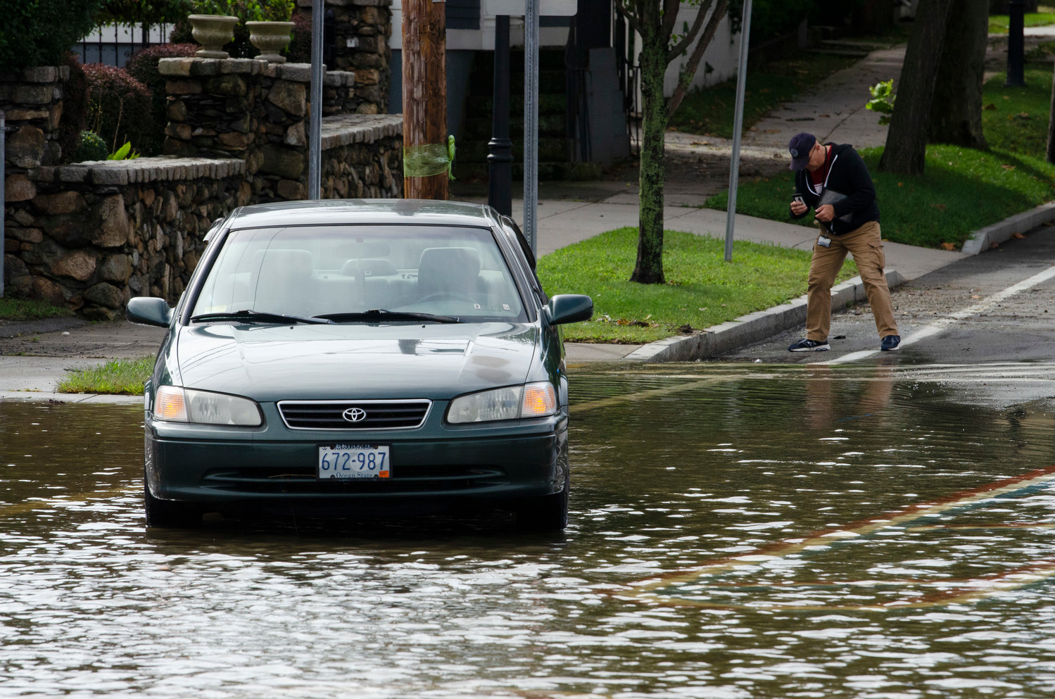 A man takes photographs as a stuck vehicle sits in the flooded water on Hope Street.