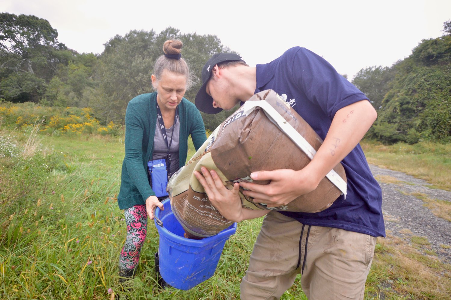 Susan Vogl, director of social services at Ocean Tides School, holds a bucket as one of her students, Chris, pours a mix of feed and molasses to entice the cattle at Cloverbud Ranch.