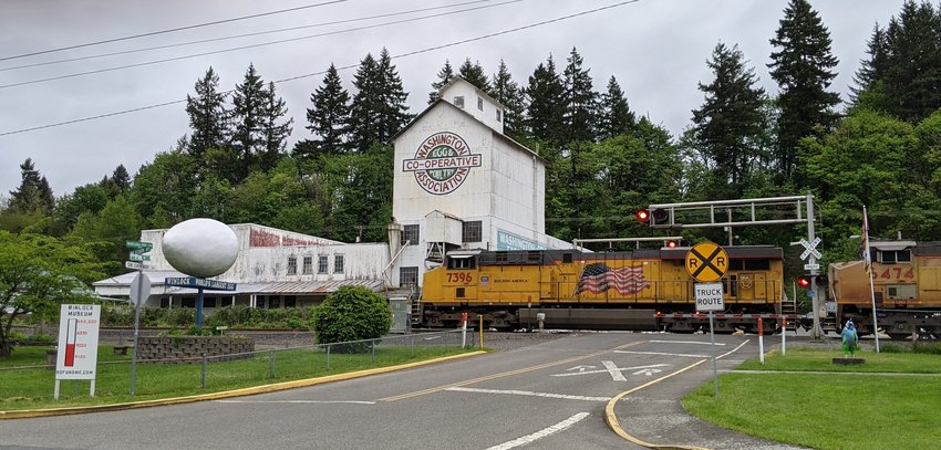 A train races past the historic Winlock hatchery and renowned giant egg in the city of Winlock. In the foreground is the painted wooden thermometer sign showing current fundraising efforts to purchase a rare Winlock history collection before it&rsquo;s too late, for the Winlock Historical Museum.