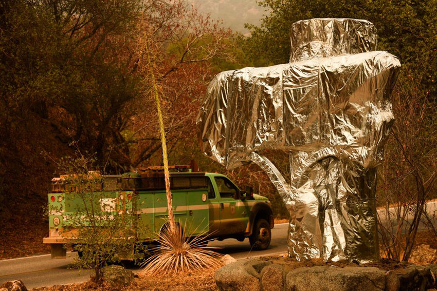 A U.S. Forest Service vehicle drives past the Sequoia National Park entrance sign wrapped in fire-resistant foil along Generals Highway during a media tour of the KNP Complex fire in the Sequoia National Park near Three Rivers, Calif., on Sept. 18, 2021.(Patrick T. Fallon/AFP via Getty Images/TNS)