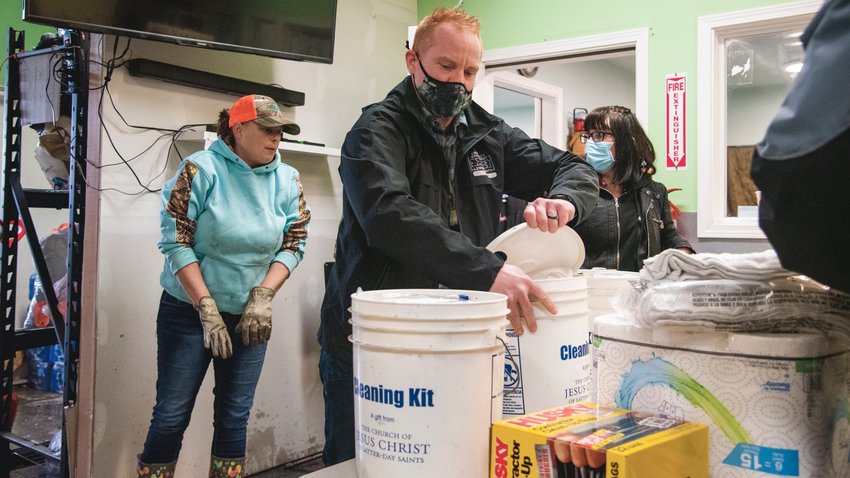 Josh Metcalf opens lids to cleaning kits from the Church of Jesus Christ of Latter-day Saints as staff and volunteers work to clear debris at Lewis County Gospel Mission on Monday, after flood waters left the building closed.